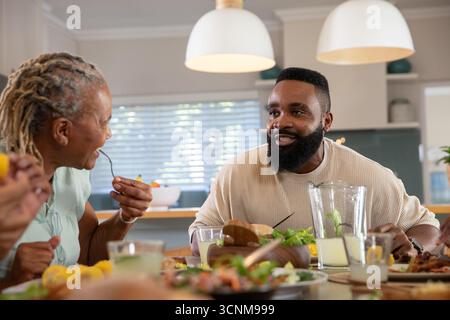 African American family gathering at dining table in kitchen passing salad bowls lemonade pitcher Stock Photo