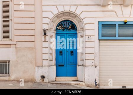 Elegant traditional Maltese townhouse facade with a bright blue wooden door, arched frame, decorative ironwork, and vintage knocker details Stock Photo
