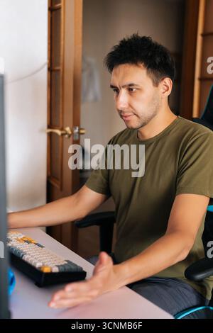 Vertical portrait of focused programmer male gesturing hand working from home using computer and keyboard looking to screen Stock Photo