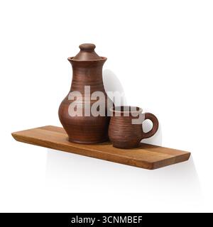 A clay jug and a mug on an oak wooden shelf, isolated on a white background, a design element, an angled view Stock Photo