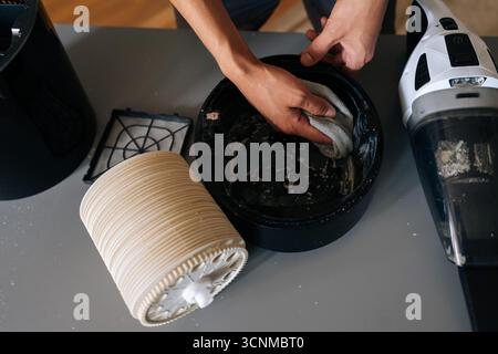 Close-up top view of technician carefully cleaning inside of air humidifier using cloth, with vacuum cleaner nearby to remove dust and debris. Stock Photo