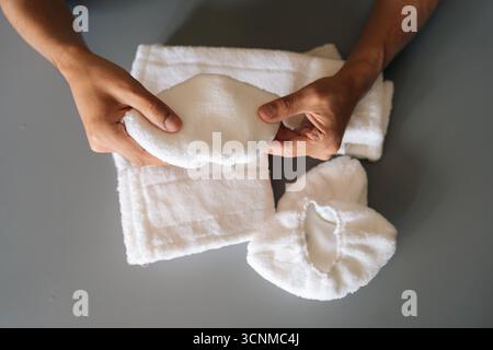 Closeup top view of man holding soft white microfiber cleaning pad, showcasing textured surface near cleaning supplies on gray background. Stock Photo