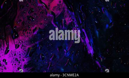Abstract wet glass surface with vivid pink and blue neon reflections, water droplets, and fluid smudges creating a vibrant light pattern. Stock Photo