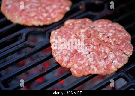 Two raw burger patties cooking on grill over glowing coals. Concept of barbecue, grilling and outdoor cooking Stock Photo