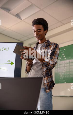 African American man presenting graph on screen in classroom while holding tablet and laptop Stock Photo