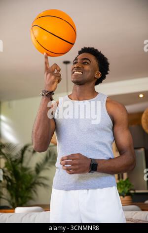 African American man spinning orange basketball on finger wearing smartwatch in living room Stock Photo