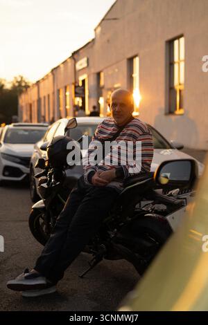 Man on a motorcycle with a sunset background, wearing a striped shirt Stock Photo