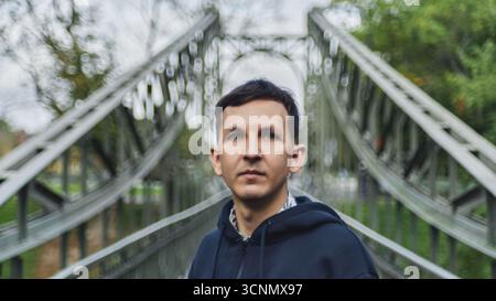 Man stands on a bridge surrounded by greenery on a cloudy day Stock Photo