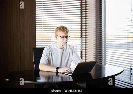 Young man working on laptop at a modern desk in bright room Stock Photo