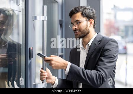 Indian businessman scanning smartphone at office entrance to unlock door with nfc contactless access, showcasing secure, modern mobile authentication Stock Photo