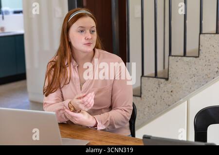 Female professional sitting at wooden table explaining project using laptop in home Stock Photo