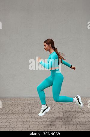 Young sportive woman, woman with beautiful body, jumping and running on gray background, female model in sportswear exercising outdoors Stock Photo
