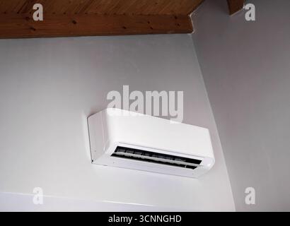White air conditioner unit mounted on a gray wall, ensuring a comfortable temperature in a room with a wooden ceiling Stock Photo