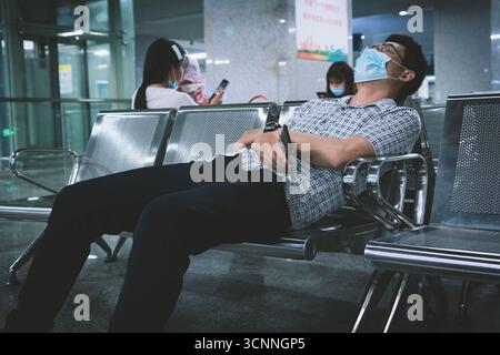 Man wearing face mask sleeping on bench in airport terminal Stock Photo