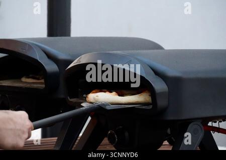 A street food vendor preparing a freshly baked pizza on an outdoor gas grill. Stock Photo