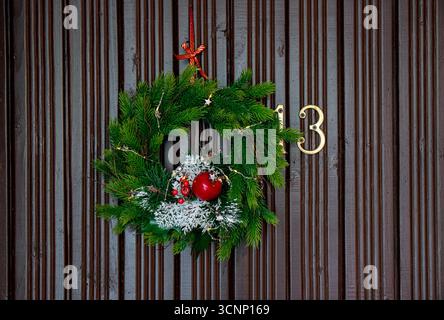Green spruce tree tip Christmas wreath with warm string lights on the home door. Minimalist traditional Christmas decoration. Stock Photo