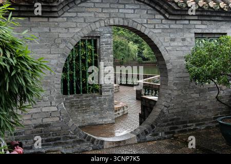 Traditional Chinese Garden with Circular Moon Gate and Water View - West Lake in Huizhou, Guangdong Province, China, is a tourist attraction featuring ancient architecture Stock Photo