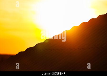 Sunset over corrugated roof. Evening sun rays shining over corrugated rooftop, warm golden light at sunset with copy space. Stock Photo