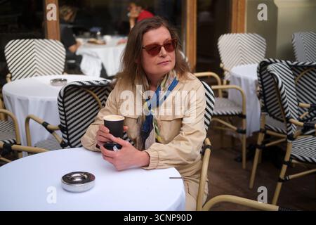 Woman sitting at cafe table with coffee cup. Caucasian female having drink at outdoor restaurant. Lifestyle moment for travel. Middle-aged woman (50 y Stock Photo