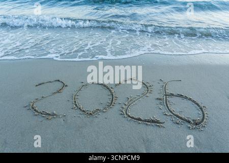 The image captures the year 2026 beautifully written in sand along the shoreline, with gentle waves lapping at the text, highlighting a serene beach Stock Photo