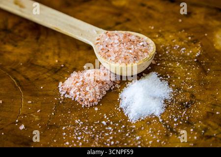 A wooden teaspoon of pink Himalayan salt with a small heap of both white fine table salt and course pink Himalayan salt Stock Photo