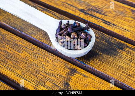 A wooden teaspoon full of whole cloves on a wooden tabletop Stock Photo