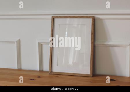 Vertical wooden picture frame poster mockup. Empty poster mock-up template on table, floor against white stucco wall background. Minimal Scandinavian Stock Photo