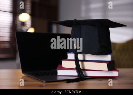 Graduation cap, laptop and stack of books on wooden table, closeup Stock Photo