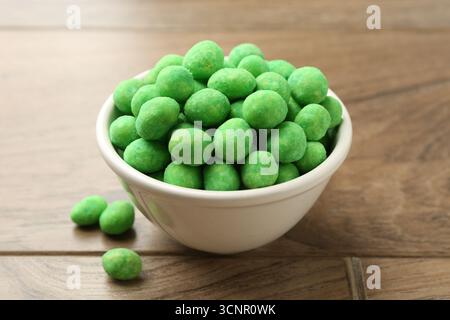 Delicious wasabi coated peanuts in bowl on wooden table, closeup Stock Photo