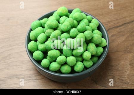 Delicious wasabi coated peanuts in bowl on wooden table, closeup Stock Photo