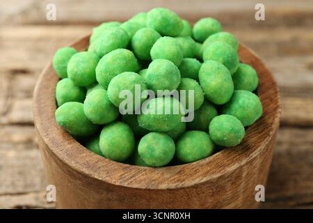 Delicious wasabi coated peanuts in bowl on wooden table, closeup Stock Photo