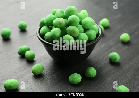 Delicious wasabi coated peanuts and bowl on dark textured table, closeup Stock Photo