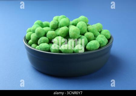 Delicious wasabi coated peanuts in bowl on blue background, closeup Stock Photo