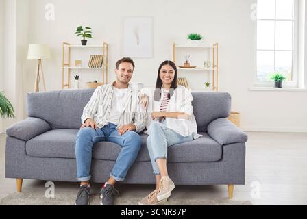Happy relaxed young family couple at home smiling new homeowners or renters sitting on big cozy sofa Stock Photo