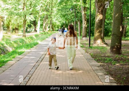 Mother and son walking holding hands during sunny summer day. Family bonding concept. Stock Photo