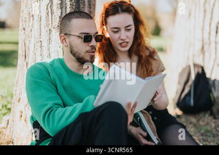 Young couple reading a book together outdoors under a tree Stock Photo