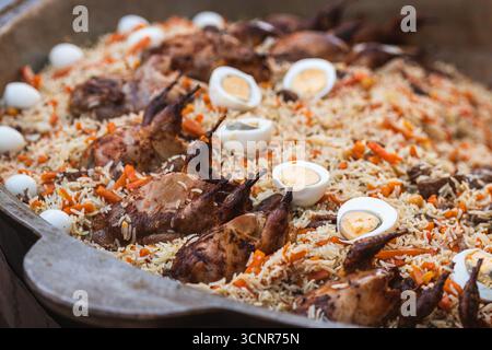 Traditional Tajik rice dish with roasted quails, carrots, and boiled eggs. Close-up of a festive plov, a signature dish of Tajik cuisine Stock Photo