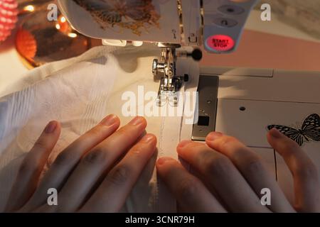 Detailed Shot of Expert Hands Using a Sewing Machine on Soft White Fabric in a Cozy Creative Studio Setting Stock Photo