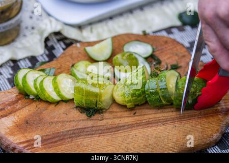 A close-up image of a person slicing fresh pickles cucumbers on a rustic wooden cutting board Stock Photo