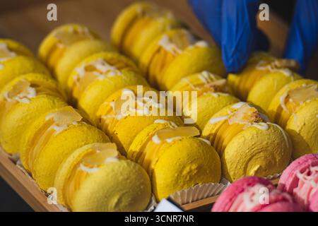 Close-up of yellow macarons arranged in rows on display. Colorful French dessert with cream filling, decorated with icing and toppings Stock Photo