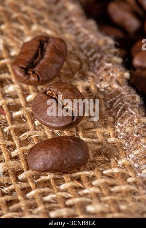 This close-up image showcases a collection of rich, roasted coffee beans beautifully arranged on a textured burlap napkin. Perfect for coffee lovers a Stock Photo