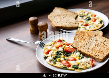Omelette with salad, toast, and tomatoes served on plate near salt shakers, rustic homemade breakfast arrangement. Stock Photo