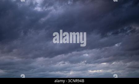 Dark storm clouds covering the sky before rainfall, moody weather background with dramatic cloud texture and atmospheric depth. Stock Photo