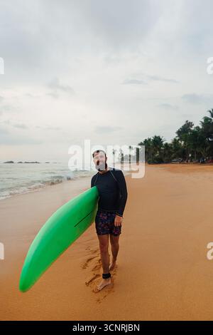 Surfer holding surf board on the beach at sunset. Happy man guy having fun doing extreme sport Stock Photo