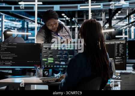 Data center manager supervising engineer setting up machine learning systems handling information. Supervisor oversees worker training node trees neural networks to improve server hub operations Stock Photo