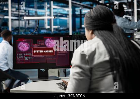 System administrator in server room seeing warning on PC alerting of sensitive data threatened by hacking attack. Woman afraid of cyberattack, struggling to save data center from unauthorized access Stock Photo