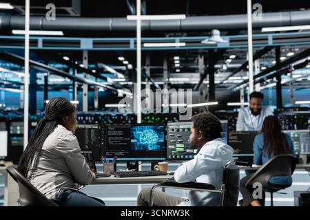 Developer with paraplegia and manager inspect neural network data center used for machine learning. Inclusive workplace worker and supervisor optimize server hub for artificial intelligence workloads Stock Photo