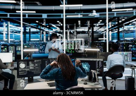 Fatigued data center worker stretching at desk, using machine learning algorithms to analyze datasets. Tired server farm engineer relaxing muscles, using AI to recognize data patterns Stock Photo