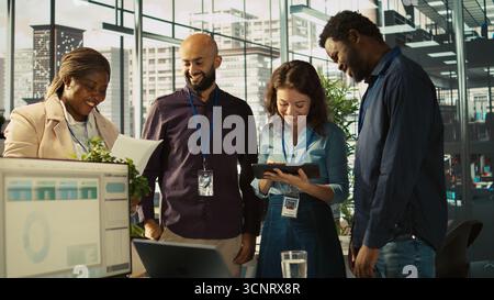 Relaxed multiethnic coworkers in office having fun chatting while reviewing documents, analyzing metrics. Smiling multiracial colleagues talking, working together, looking over paperwork, camera B Stock Photo