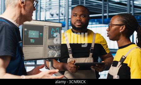 Experienced team leader doing induction to new trainees in industry 4.0 photovoltaics plant. Senior engineer in smart solar panels factory teaching interns to maximize power generation, camera A Stock Photo